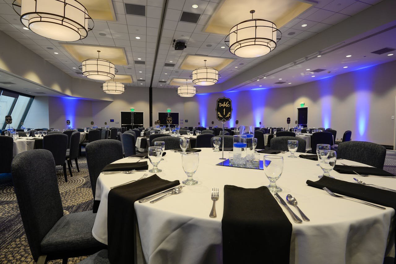 Spacious banquet hall with round tables set for an event featuring elegant lighting and decor.